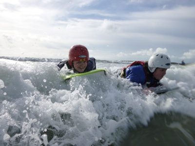 Two school students learn through adventure as they ride a wave on their body boards to a beach on anglesey